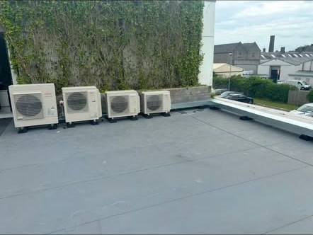 Row of four air conditioning condenser units installed on a flat roof terrace