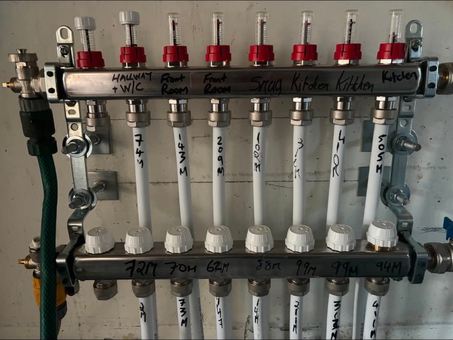 Stainless steel underfloor heating manifold with labelled circuits, flow meters and actuators