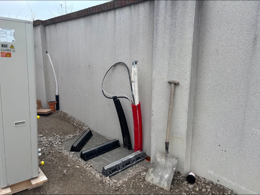 Heat pump unit awaiting installation beside first fix ducting and service conduits at a wall