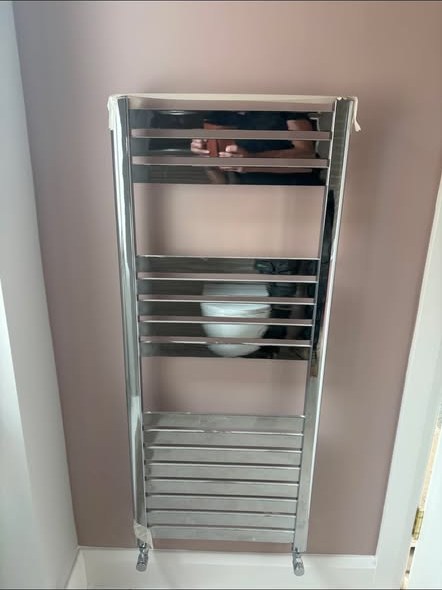 Chrome ladder style towel radiator installed on a bathroom wall