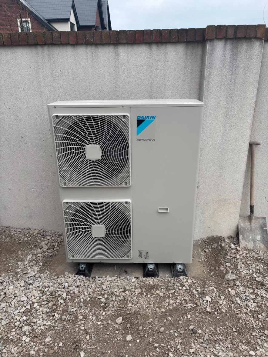 Twin fan air source heat pump outdoor unit installed on anti-vibration feet against a rendered wall
