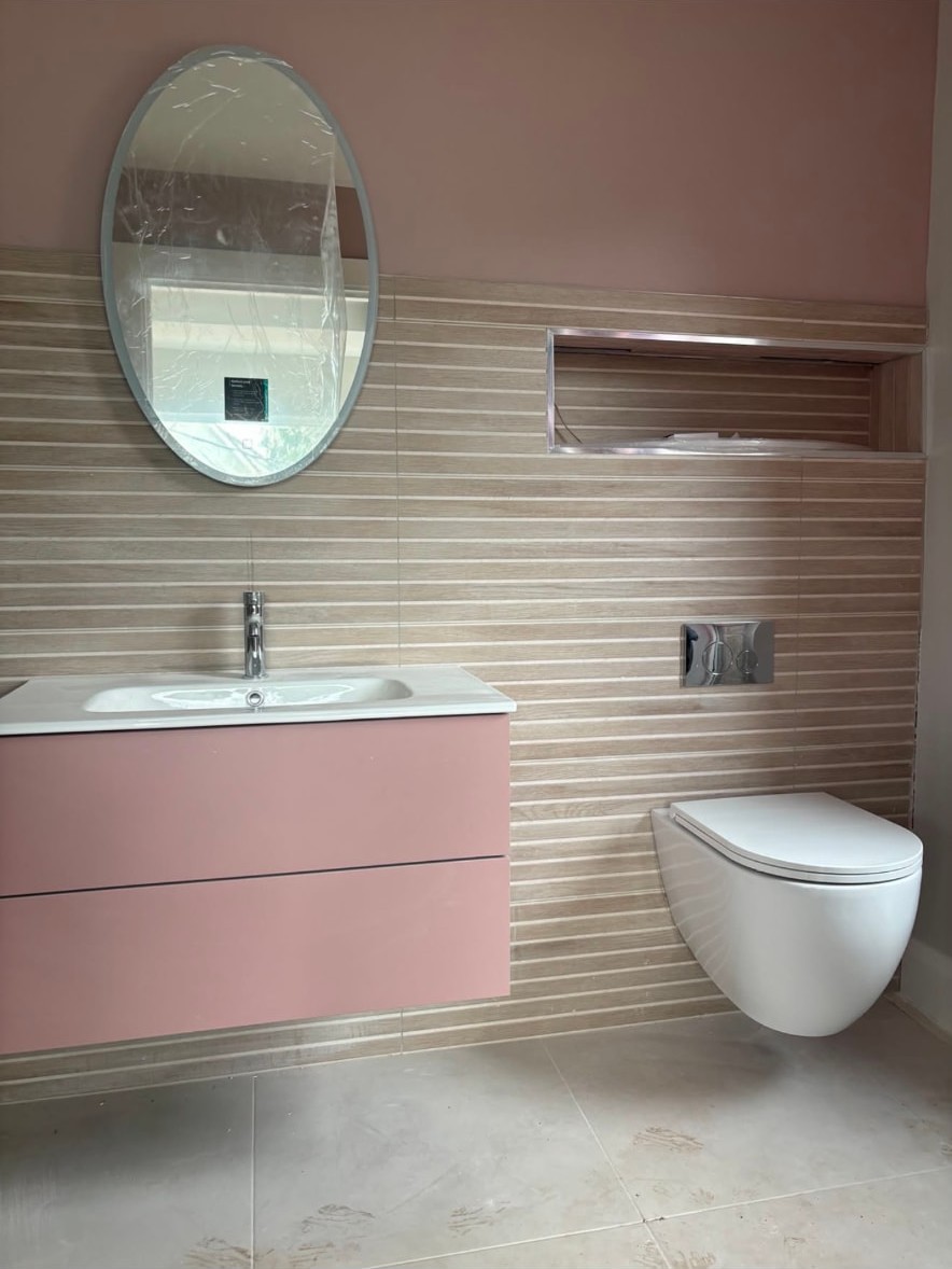 Bathroom with a pink wall hung vanity unit, oval mirror and wall hung WC